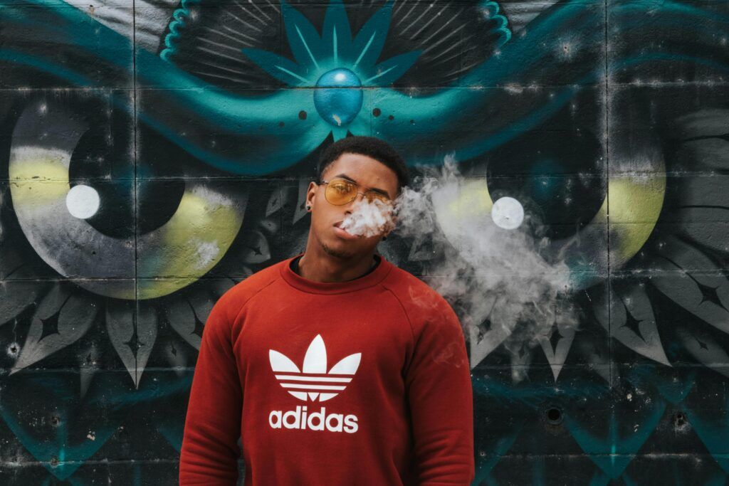 Young man smoking against vibrant graffiti wall, expressing urban street style.