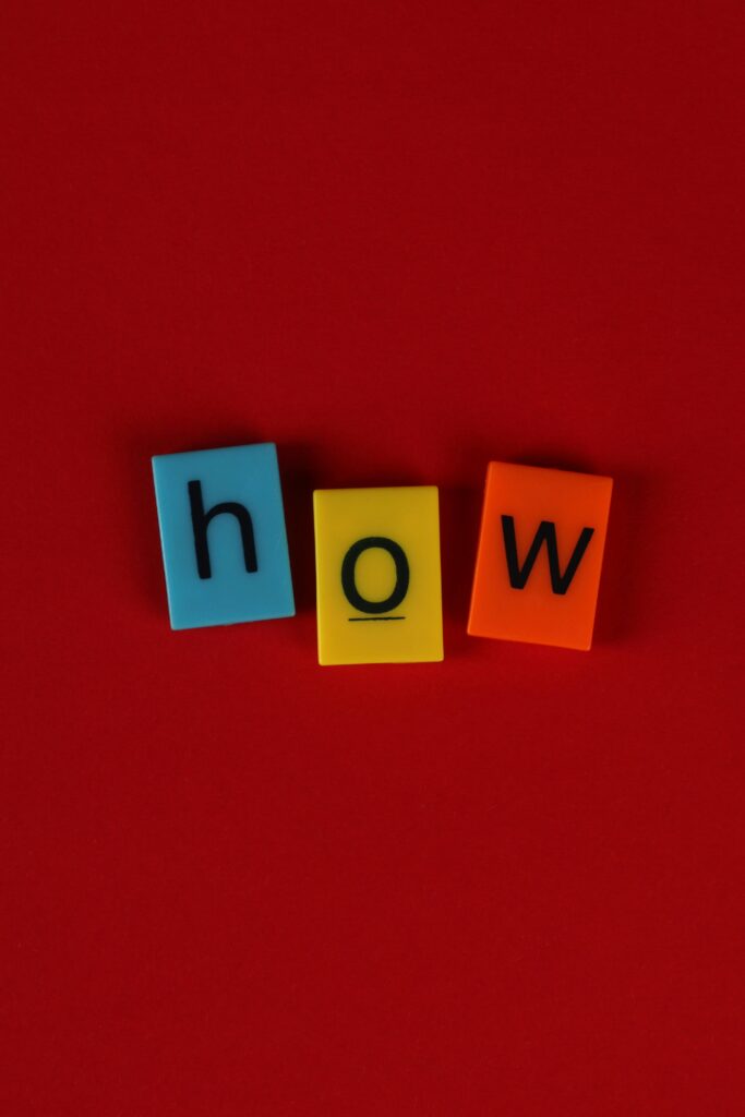 Playful arrangement of colorful letter tiles spelling 'how' on a vivid red background.